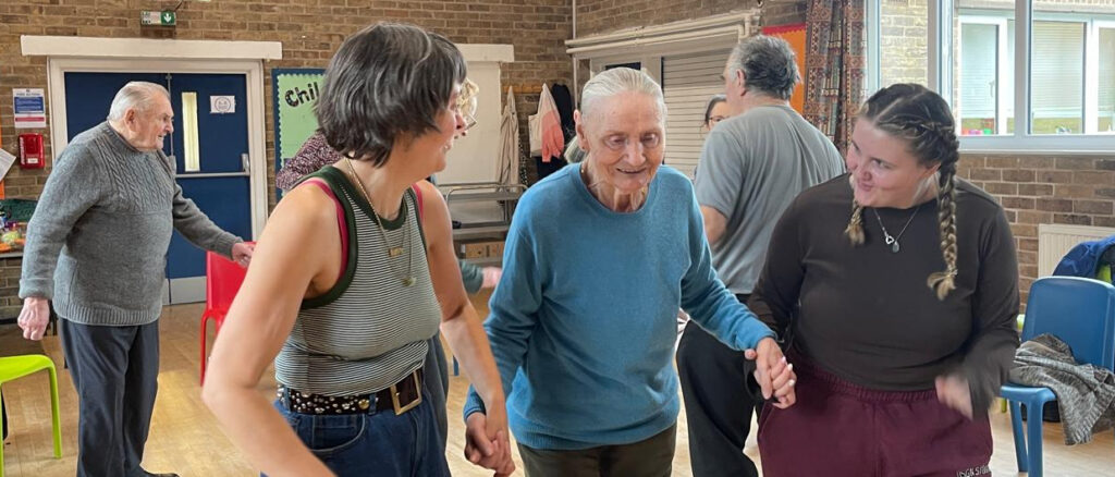 an elderly lady accompanied by two women who are taking part in a community music and dance session.