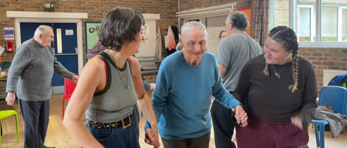an elderly lady accompanied by two women who are taking part in a community music and dance session.